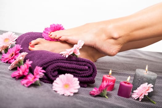 beautiful well-groomed female feet with red nail polish and flowers on towel close up wellness pedicure salon