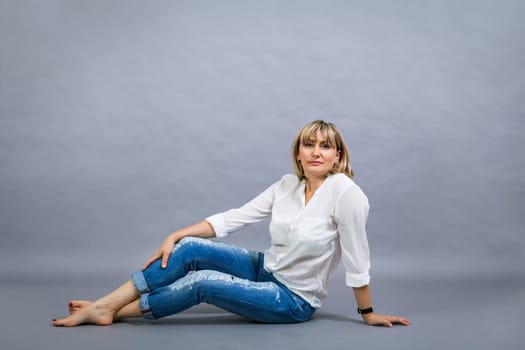 adult blonde attractive woman with blue jeans and white blouse against grey background fashion trendy