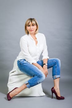 adult blonde attractive woman with blue jeans and white blouse against grey background fashion trendy
