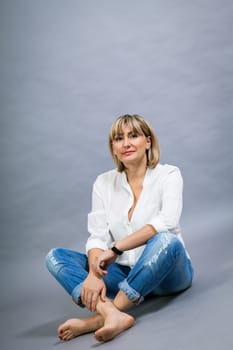 adult blonde attractive woman with blue jeans and white blouse against grey background fashion trendy