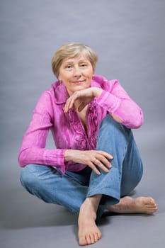 happy older woman seniorwith light hair and fold with pink blouse against grey background healthy