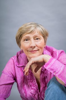 happy older woman seniorwith light hair and fold with pink blouse against grey background healthy