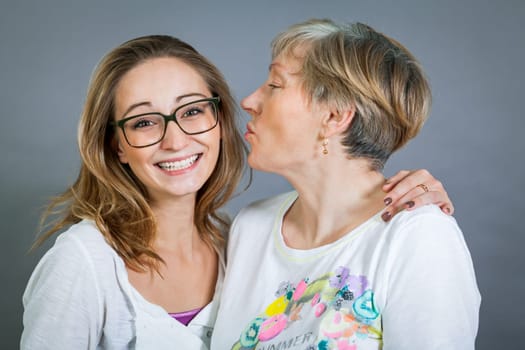laughing young granddaughter with happy grandmother portrait against grey background