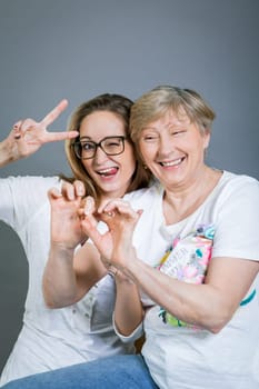laughing young granddaughter with happy grandmother portrait against grey background