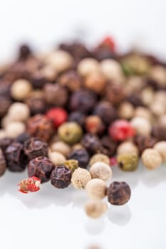 Background of whole fresh dried black peppercorns scattered on a white surface for use as a pungent spice and flavouring in cooking