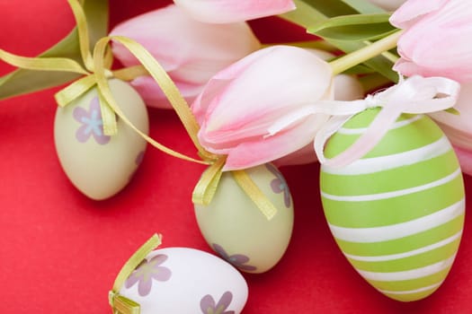 pink tulips decorated with easter eggs as a close-up with text space on a red background