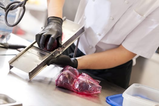 cook rubs fresh red beetroot on rub with gloves to protect against stains in the restaurant kitchen preparation eat