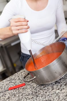 female chef in the restaurant kitchen gastronomy pureed passes tomatoes to a sauce puree tomato sauce