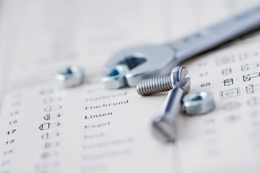 Detailed view of a small mouth wrench with screws and nuts in front of it on the book page of an old table book