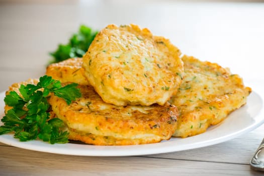 cooked fried potato cutlets with herbs, in a plate on a wooden table.