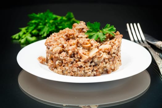 cooked buckwheat boiled with mushroom filling in a plate isolated on a black background.