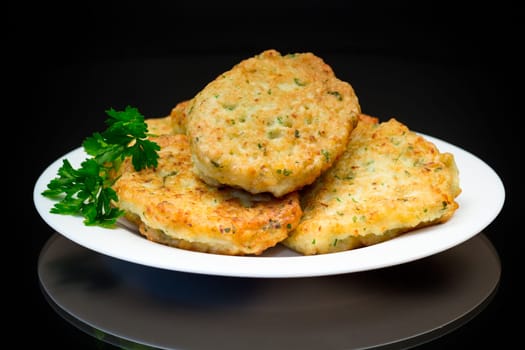 cooked fried potato cutlets with herbs, in a plate isolated on a black background.