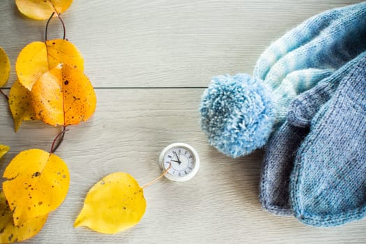 Autumn foliage, winter mittens and a clock on a wooden table. Change to winter time.