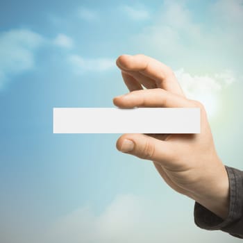 One hand holding a blank card with a blue sky at the background with clouds and sun. Communication concept for Business or Marketing
