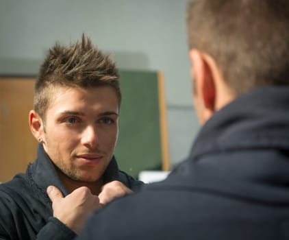 Handsome young man looking at himself in mirror with a grin
