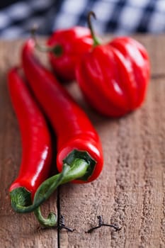Closeup of long and round red chili peppers resting on wooden board surface