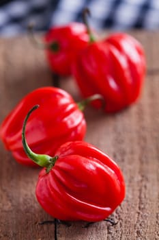 Closeup of four round red chili peppers on wooden board surface