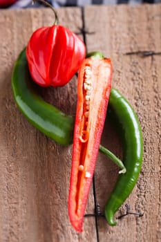Closeup of whole and sliced red and green chili peppers on wooden board surface