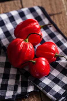 Closeup of four round red chili peppers on checkered napkin resting on wooden board