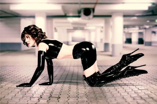 Adult woman wearing black shiny latex dress and overknee boots with extreme ballet heels.