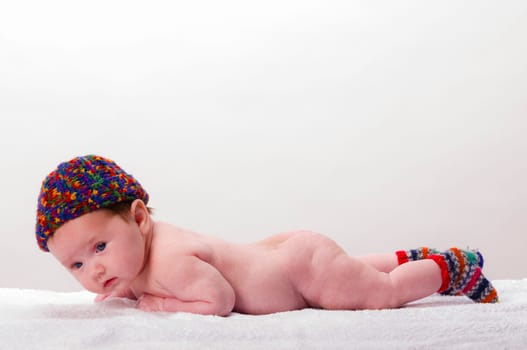 Sweet newborn baby wearing a colorful woolen cap and smiling, isolated against a white background.