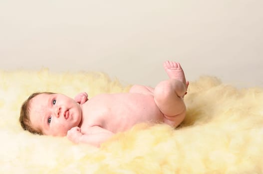 A little newborn baby lies on a sheepskin.