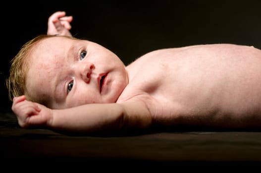 Newborn baby (6 weeks) struts contentedly and looks cute into the camera,exposed against a dark background.