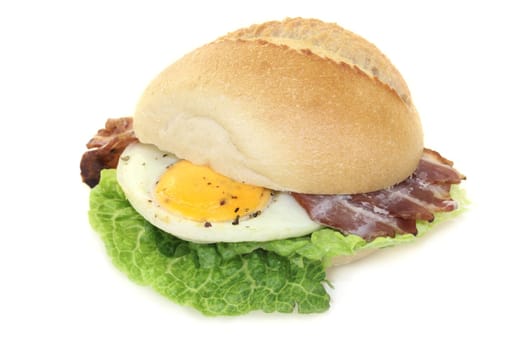 a bun covered with fried egg,bacon and salad