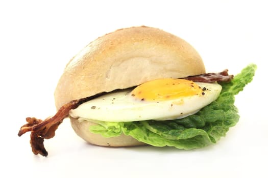 a bun covered with fried egg,bacon and salad