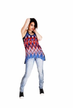 A tall young woman in blue jeans and a colorful dress standing for white.background with her hands behind her head..