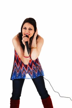 A young pretty woman in jeans and a nice dress standing with a microphone.in her hand singing for white background..