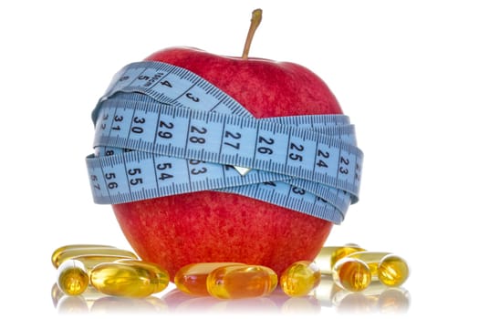 Apple wrapped by measuring tape and fish oil pills on white background