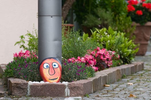 Flower bed on a residential building with painted face on a stone in summer