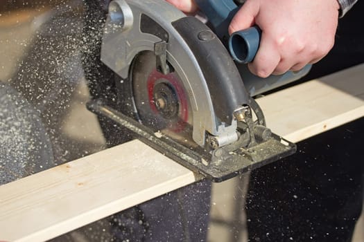 Closeup view of a man that is cutting wooden board electric circular saw