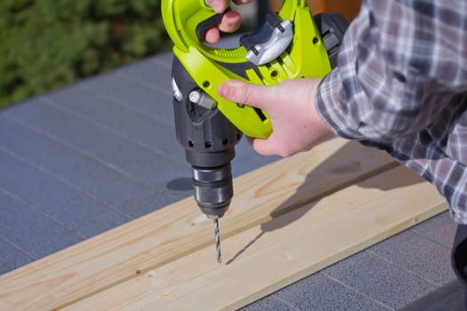 Handyman in plaid shirt is drilling  into a wooden board