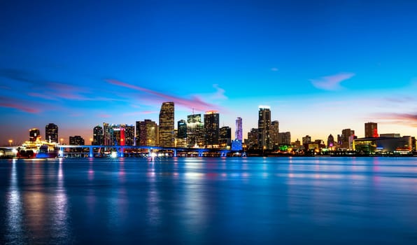 Miami city skyline panorama at dusk with urban skyscrapers over sea with reflection