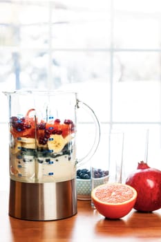 Healthy smoothie ingredients in blender with fresh fruit ready to blend on kitchen table
