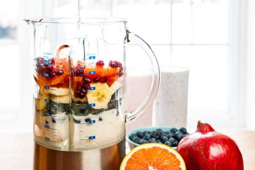 Prepared smoothies and healthy smoothie ingredients in blender with fresh fruit ready to blend on kitchen table