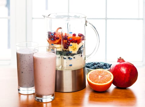Prepared smoothies and healthy smoothie ingredients in blender with fresh fruit ready to blend on kitchen table