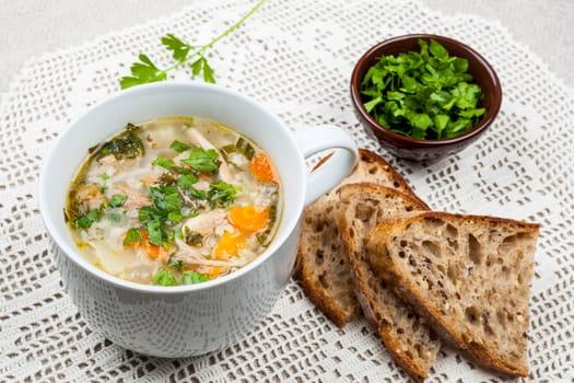 Cup of hot chicken rice soup served with bread and parsley on crochet tablecloth