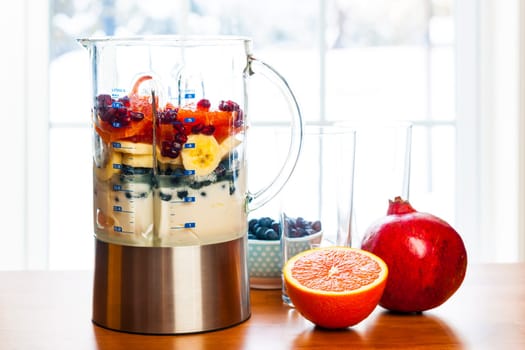 Healthy smoothie ingredients in blender with fresh fruit ready to blend on kitchen table