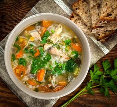 Chicken rice soup with vegetables in bowl and bread from above closeup