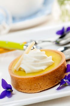 Fresh gourmet lemon dessert tart with edible violet flowers garnish