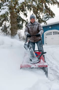 Man using snowblower to clear deep snow on driveway near residential house after heavy snowfall.