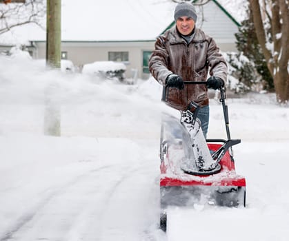 Man using snowblower to clear deep snow on residential driveway after heavy snowfall