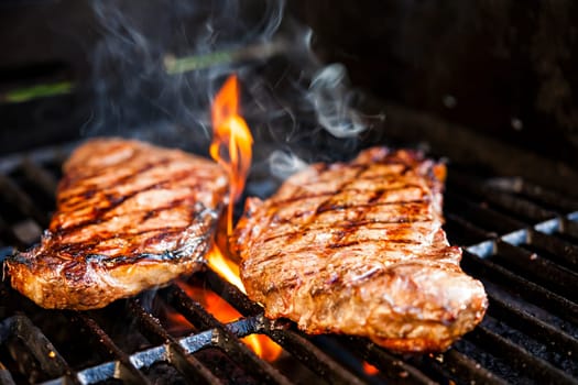 Beef steaks cooking in open flame on barbecue grill