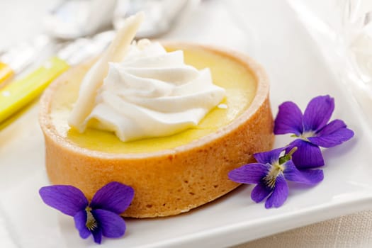 Fresh gourmet lemon dessert tart with edible violet flowers garnish