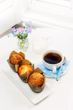 Three muffins and cup of coffee on breakfast table in the morning