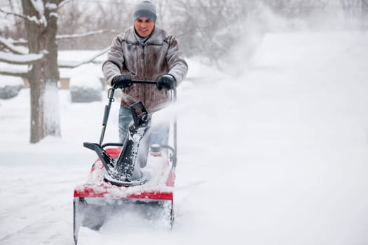 Man using snowblower to clear deep snow on residential driveway after heavy snowfall
