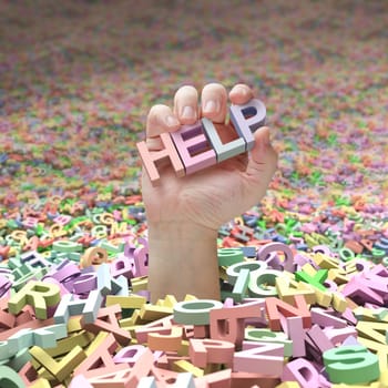 In the middle of an ocean of letters, a hand going up and holding the word help. Concept of the difficulty of finding success in the midst of so many possibilities.